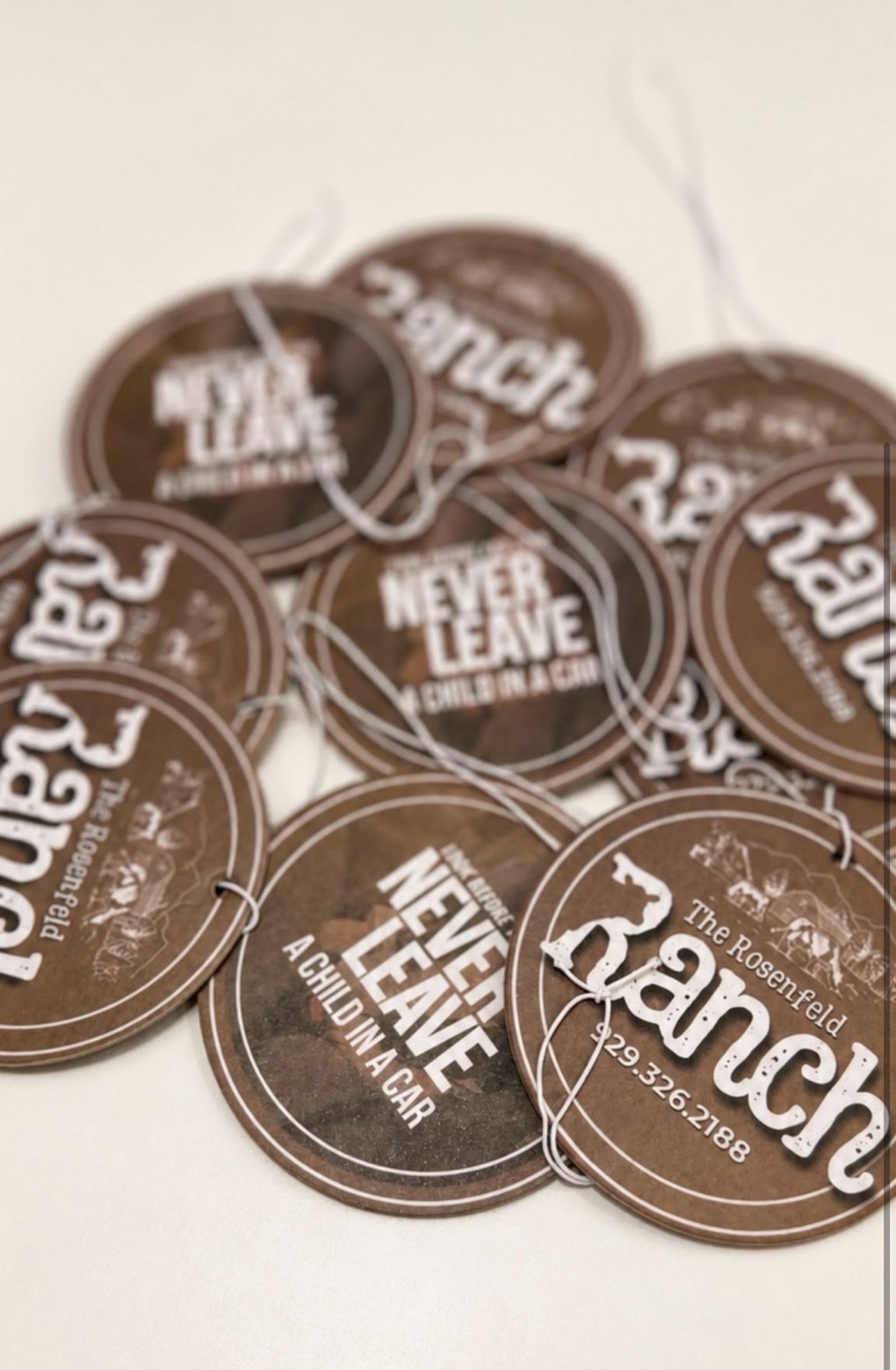 Brown Rosenfeld Ranch air fresheners reading Never Leave A Child In A Car, with the ranch logo and phone number